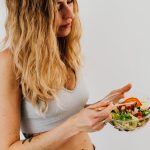 A caucasian woman in a sports bra enjoying a fresh salad, embodying healthy eating and lifestyle.